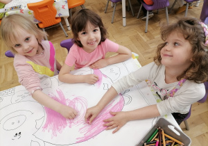 Trzy dziewczynki kolorują obrazek świnki.
